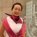Guohua Sun, Ph. D. A woman with glasses, Guohua Sun, Ph. D., smiling next to a wall with a logo.